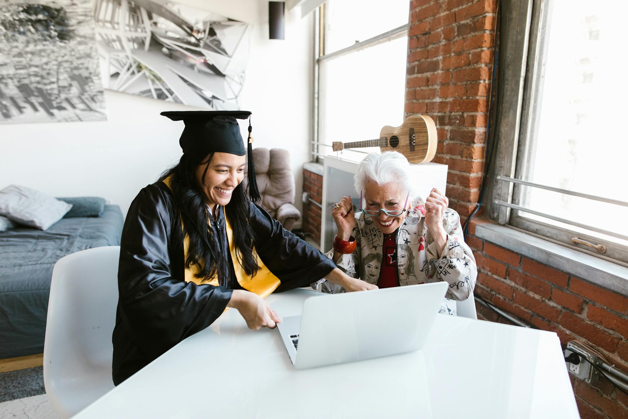 A young woman in a graduation gown celebrates her graduation virtually with an elderly woman.